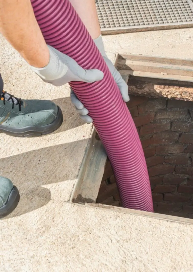 Person wearing gloves inserts a purple hose into an open manhole.