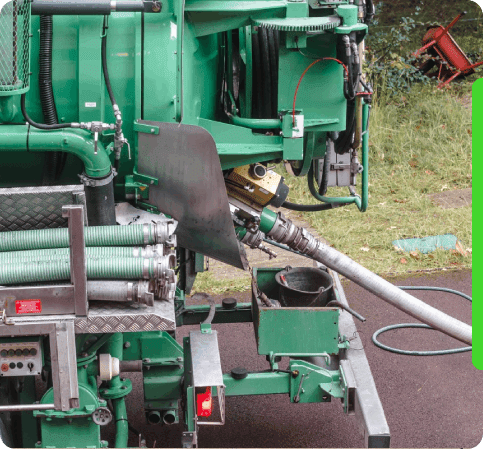 Green industrial machinery with various hoses and components, positioned outdoors on a grassy area with some paved surface visible.